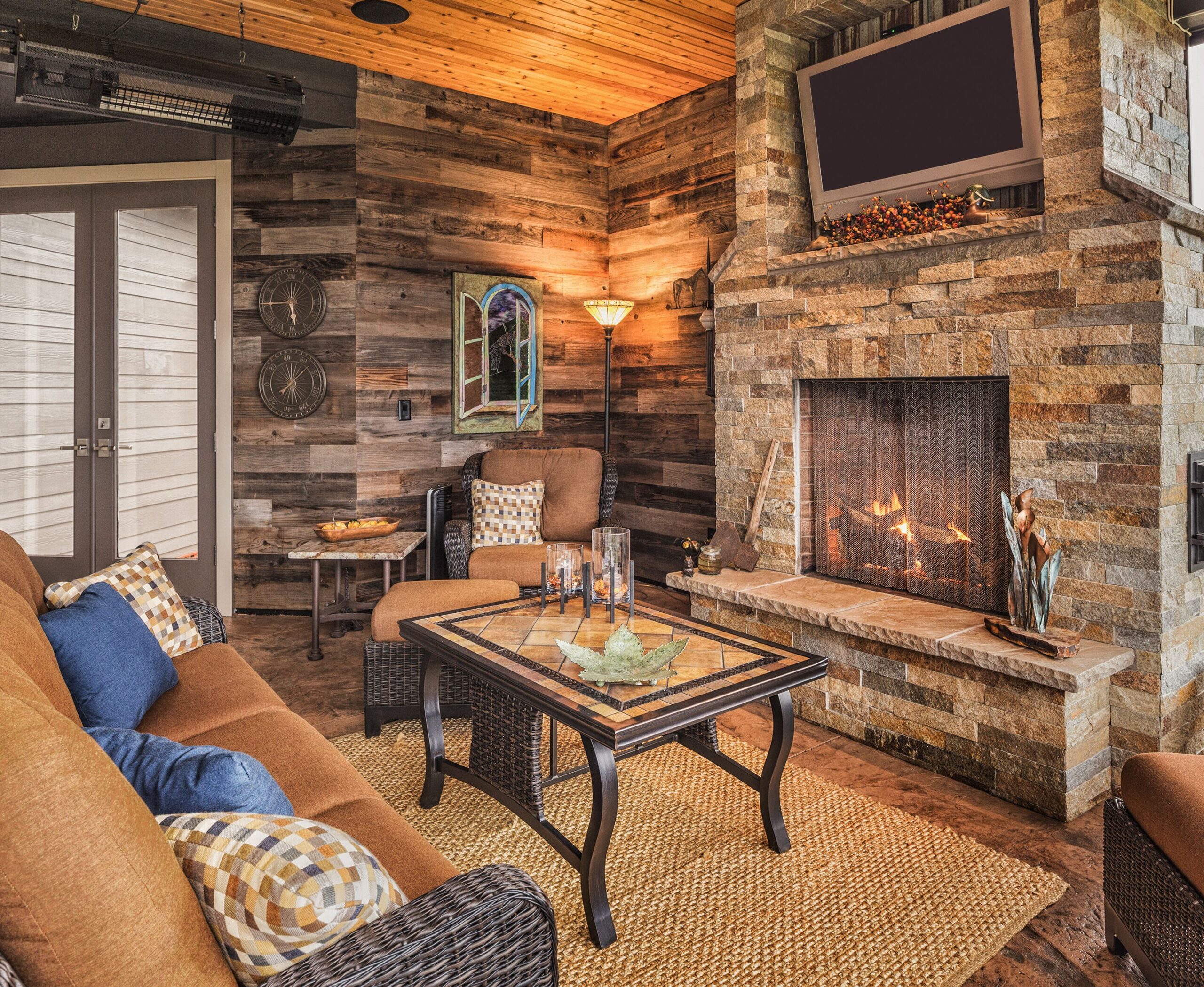 Cozy sitting room with wooden walls and ceiling, stone fireplace, and wicker furniture.