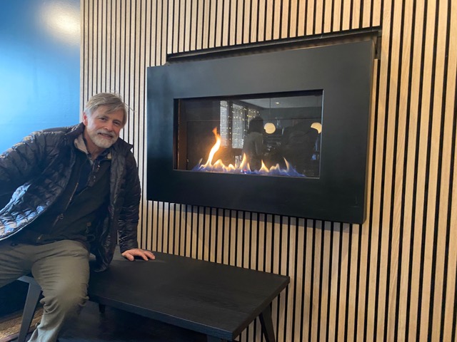 A man sitting comfortably in front of a warm, glowing fireplace